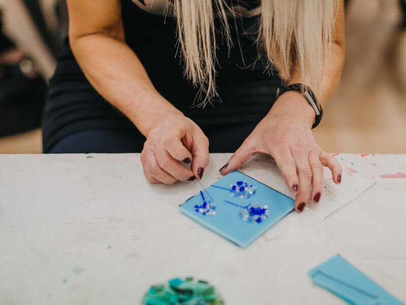 Close up of woman making blue flowers in a glass fusion class.